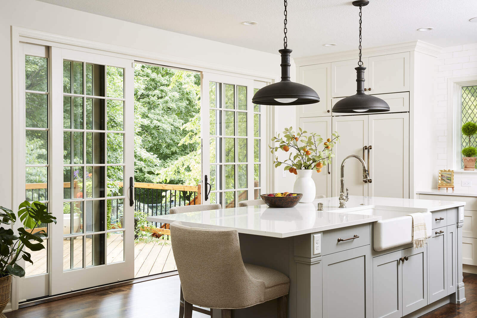 Bright white kitchen with a large island, farmhouse sink, and French doors to a deck by MA Peterson, Twin Cities