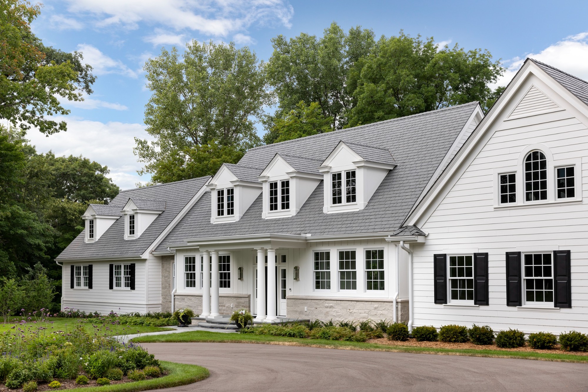 angled front exterior with dormer windows and black shutters on custom home in wayzata mn